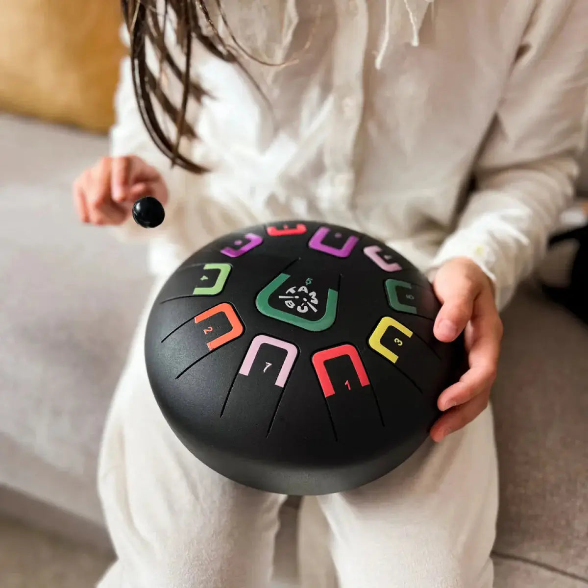 Kind spielt mit buntem Musikinstrument aus Metall mit Schlägel auf dem Schoß sitzend