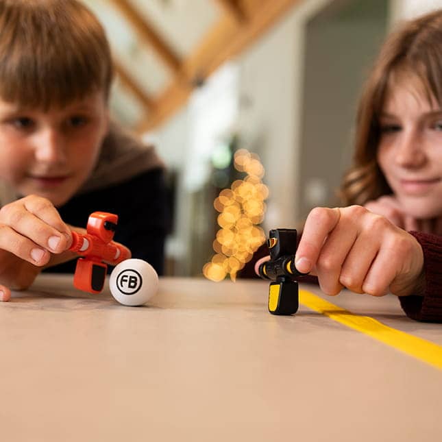 Kinder spielen mit kleinem Tischfußballspiel als Spielzeug ab 6 Jahren zur Förderung von Geschicklichkeit