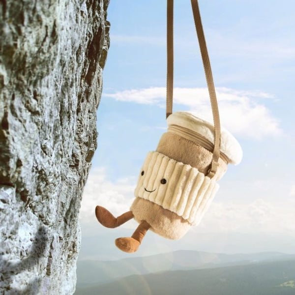 Jellycat Coffee-to-go-Tasche hängt am Riemen vor Himmel und Felsen