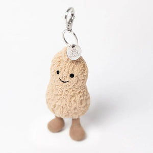 Jellycat Erdnuss-Anhänger mit Gesicht und braunen Cord-Füßchen vor hellem Hintergrund