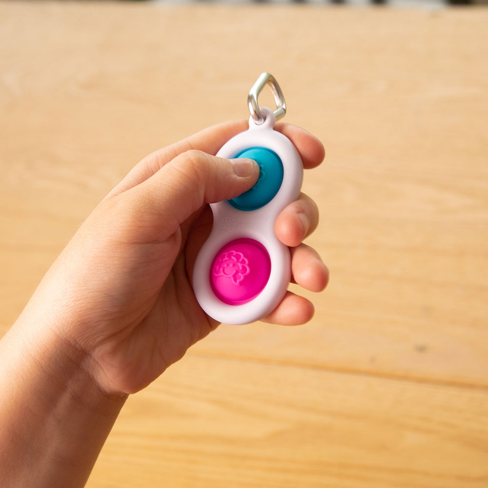 Eine Hand hält den Dimpl Blasen Schlüsselanhänger von Fat Brain Toys zum Drücken und Spielen. Dimpl Blasen Schlüsselanhänger kaufen.