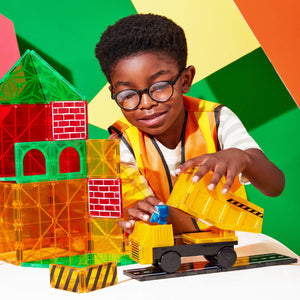 Ein Junge im Sicherheitshemd spielt mit Magnetbausteinen für Kinder und baut ein buntes Haus