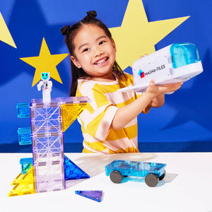 Ein Mädchen spielt mit MAGNA-TILES Magnetbausteine Kosmos Set und einem blauen Auto